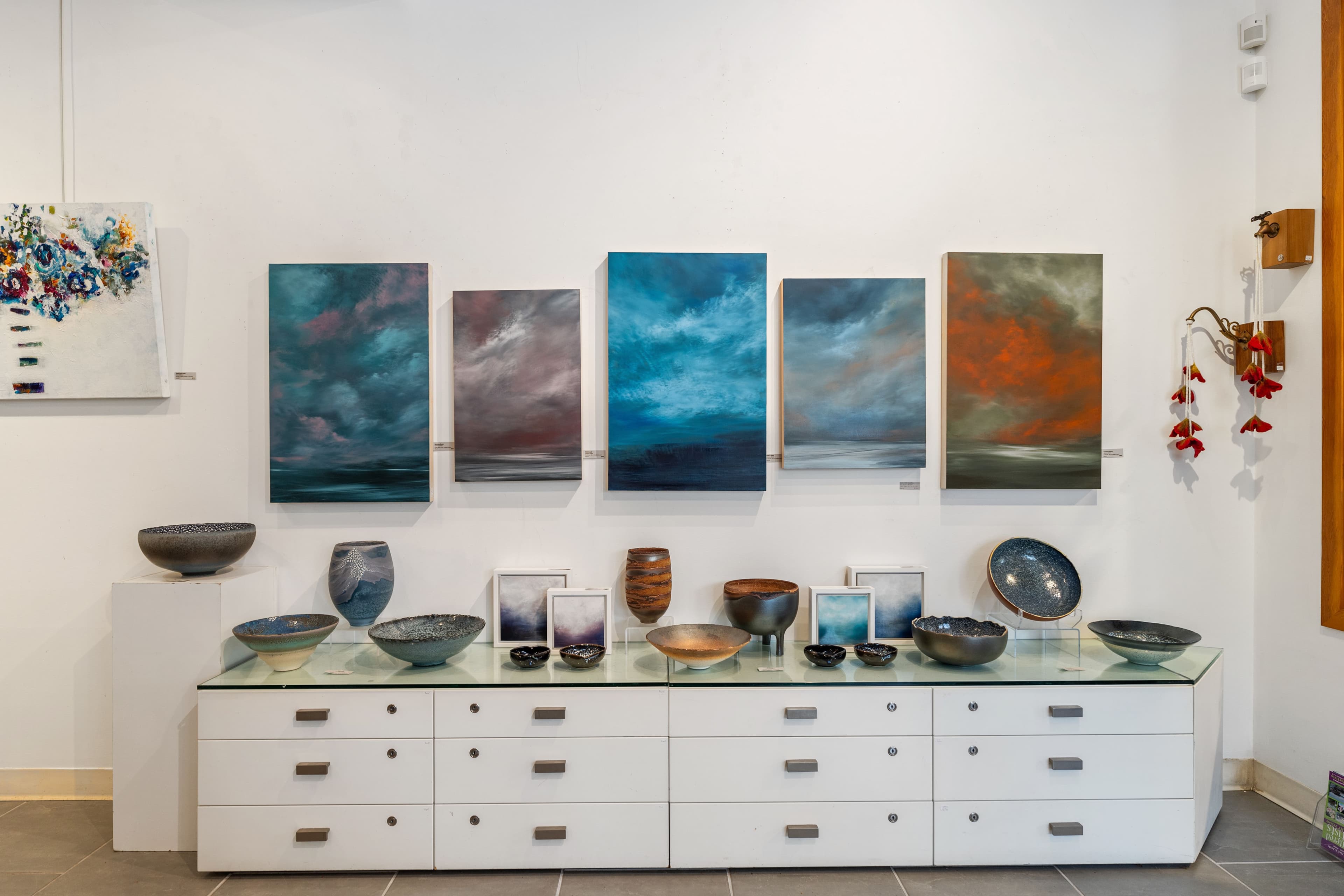 Wall-mounted seascape painting series above a row of artist-made ceramic bowls and vases