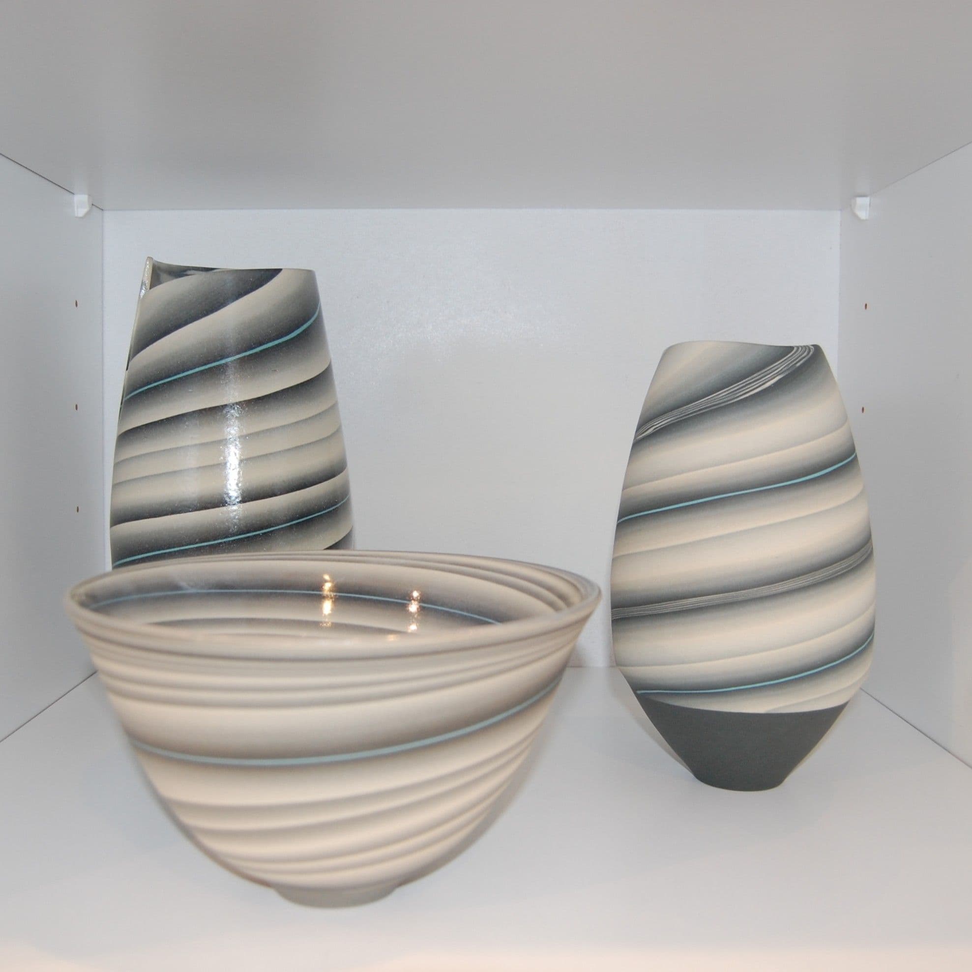 Three contemporary striped ceramic vessels on a white display shelf