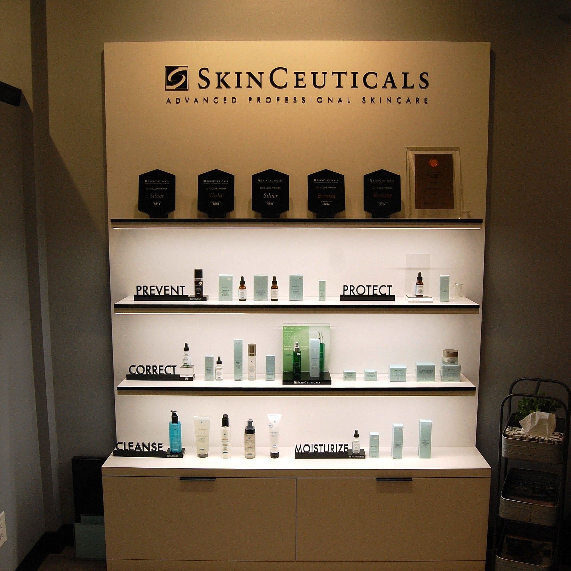 SkinCeuticals product wall with elite-partner award plaques and Prevent / Protect / Correct / Cleanse / Moisturize shelves
