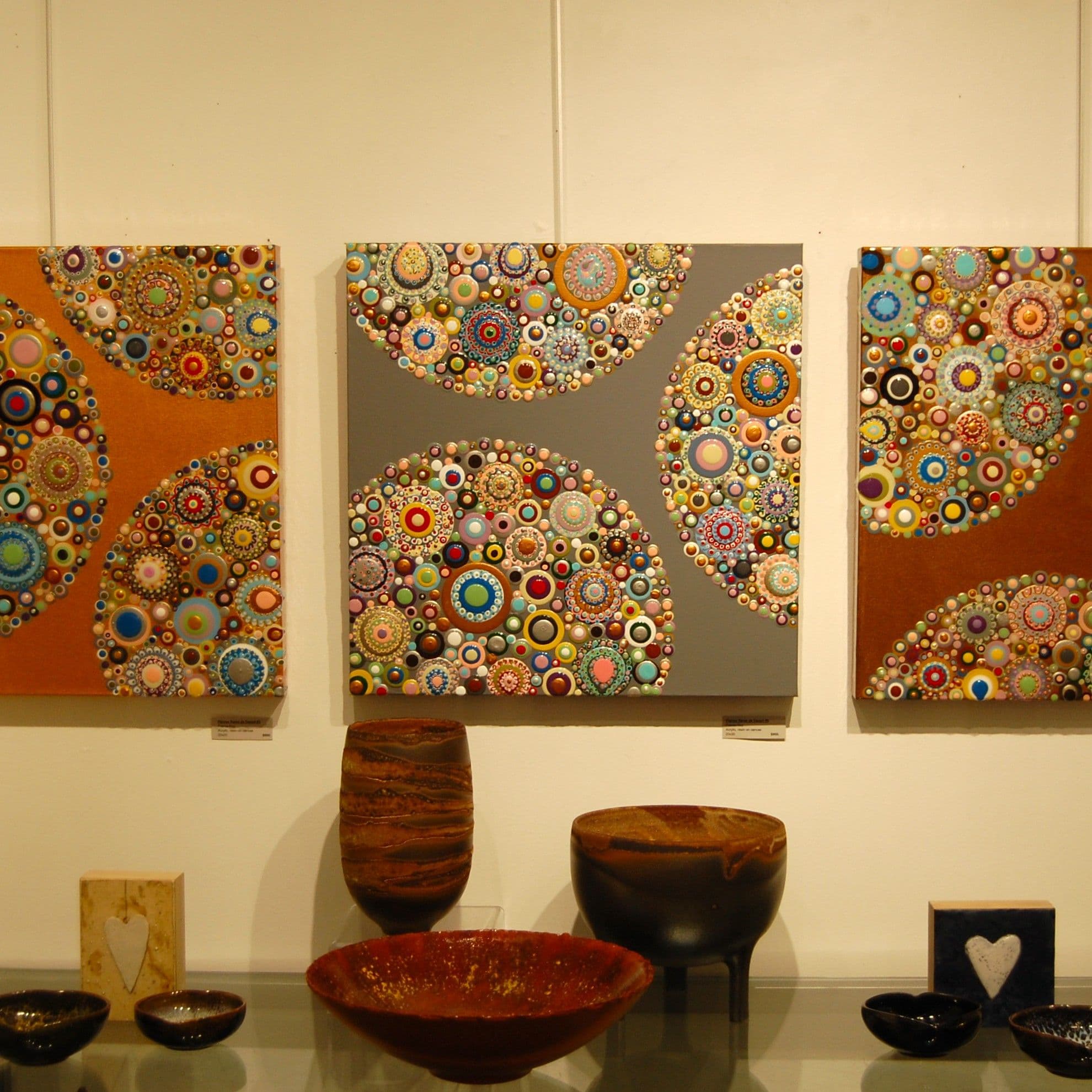 Trio of mosaic-pattern paintings above a row of handcrafted bowls